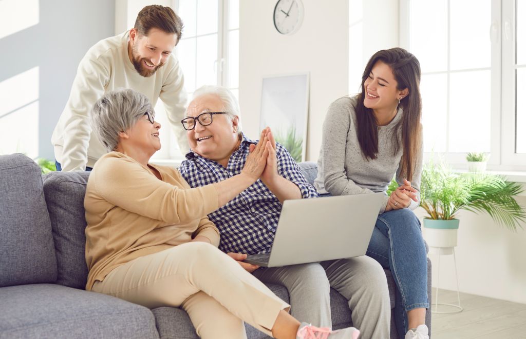 A multigenerational family at home together, parents and adult children laughing on the sofa